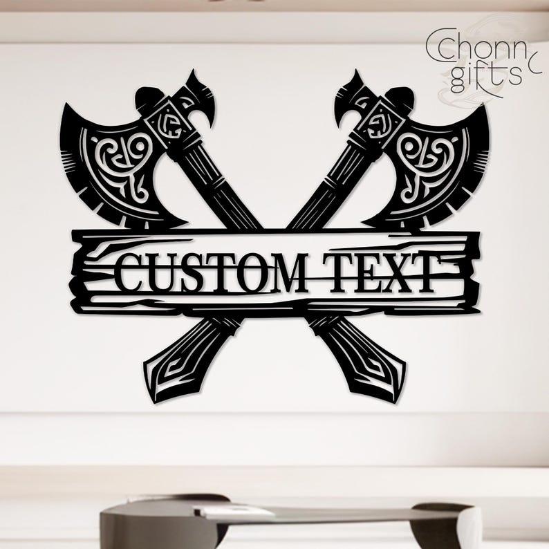 May include: Black metal wall art featuring two crossed axes with ornate detailing. A wooden plank with the words "CUSTOM TEXT" is centered between the axes. The design includes the text "Chonn gifts" in the upper right corner.