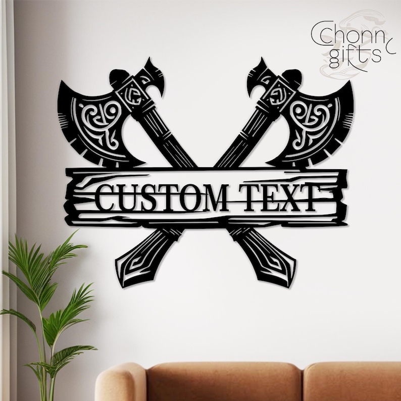May include: Black metal wall art featuring two crossed axes with ornate detailing. A horizontal plank in the center displays the text "CUSTOM TEXT". The axes have decorative patterns and are set against a white background.