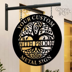Może przedstawiać: Czarny metalowy znak z motywem drzewa życia, zawieszony na czarnym wsporniku i łańcuchu. Znak zawiera napis "YOUR CUSTOM WITH PROOF METAL SIGN" białymi literami. Okrągły znak ma dekoracyjną obwódkę.