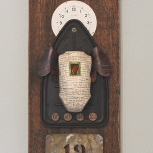 May include: A wooden wall plaque with a vintage iron, a clock face, and a number "19" on a metal tag. The iron is decorated with a piece of paper with a red heart.