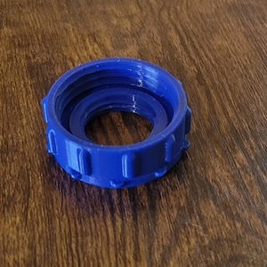 May include: A vibrant blue, circular plastic component with a threaded interior and exterior ridges. The object has a central opening and is designed for a secure fit. The component is likely a part of a larger assembly.