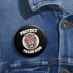 May include: A black button with a white border and the text "Protect Trans Kids" in white. A colorful tiger illustration is inside a circle in the center of the button.