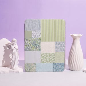 May include: A patchwork-style tablet case with a variety of patterns in shades of green, blue, and white. The case features stripes, floral designs, and textured squares. The case is rectangular and appears to be made of a durable material.