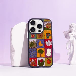 Op de afbeelding: Een kleurrijke telefoonhoes met een patchwork-ontwerp. De hoes heeft een donkerblauwe rand en een raster van vierkanten met illustraties van een huis, beer, maan, boom en andere grillige elementen.