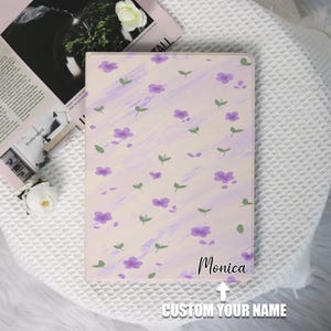 May include: A light pink and purple floral iPad case with the name "Monica" printed on the bottom right corner. The case has a customisable name field below the printed name.