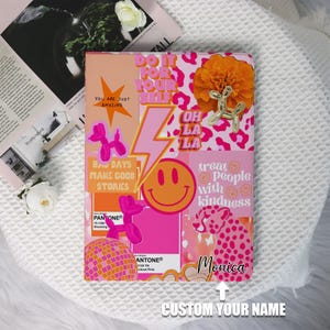 May include: A pink and orange notebook cover with a collage of stickers. The stickers include a smiley face, a cheetah print, a lightning bolt, a rainbow disco ball, and the text "Do it for your self", "Oh la la", "Bad days make good stories", "Treat people with kindness", and "Monica".