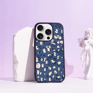 May include: A navy blue phone case featuring a playful design of white cartoon characters and items. The case has a dark blue edge and a camera aperture. The backdrop is a light purple.