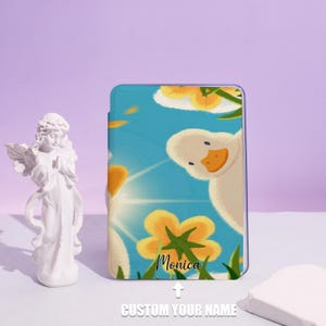 May include: A blue case with a cartoon duck design, yellow flowers, and a sunny sky. The name "Monica" is printed on the case. The words "CUSTOM YOUR NAME" are printed below the name.