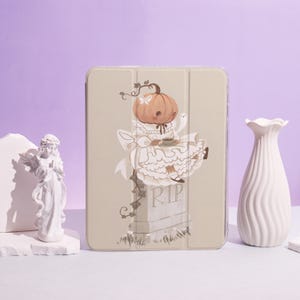 Könnte beinhalten: Eine beige Tablet-Hülle mit einer skurrilen Illustration einer kürbisköpfigen Figur in einem weißen Kleid, die eine Teetasse hält, mit einem Geist und einem Grabstein mit der Aufschrift "RIP". Die Hülle hat eine transparente Abdeckung.
