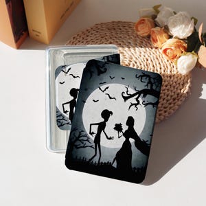 May include: A clear plastic case holding two decorative cards. The cards feature a black and white silhouette design of a couple in front of a full moon, with bats and trees. The design has a spooky, Halloween theme.
