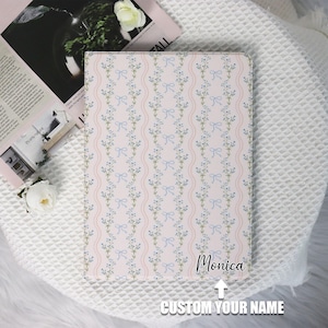 May include: A pink and white patterned iPad case with a blue and white floral design. The text "Monica" is printed on the case. The text "CUSTOM YOUR NAME" is printed below the case.