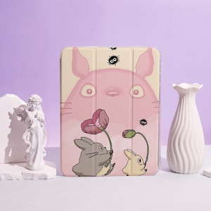 Pode incluir: Uma capa de tablet rosa com uma ilustração de desenho animado de um personagem grande e rosa e dois coelhos pequenos segurando flores. A capa tem um fundo rosa claro e uma capa protetora.