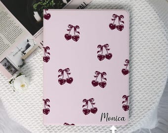 May include: A pink notebook cover with a repeating pattern of cherries. The text "Monica" is printed on the cover, with space below for "CUSTOM YOUR NAME".
