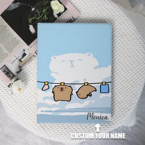 Könnte beinhalten: Eine blaue und weiße illustrierte Tablethülle mit einem weißen Bären, zwei braunen Bären und einer blauen Wolke. Der Text "Monica" ist auf der Hülle aufgedruckt. Der Text "CUSTOM YOUR NAME" ist unter der Hülle aufgedruckt.