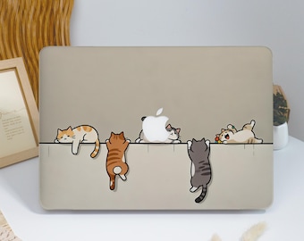 May include: A beige laptop hard shell case featuring a graphic illustration of five cartoon cats interacting with a white Apple logo. The cats are depicted in various poses, including hanging from a horizontal line and resting near the logo.