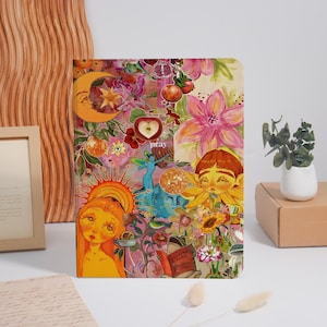 May include: A colorful journal with a collage design featuring illustrations of flowers, fruit, and celestial elements. The journal has a whimsical aesthetic with the word "pray" visible. The cover is a mix of pink, yellow, and orange.