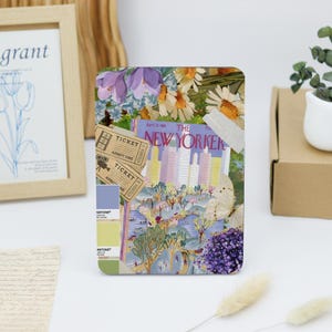 Könnte beinhalten: Eine Collage mit einem Vintage-Magazincover von "The New Yorker", Ticketstubs und floralen Illustrationen. Das Magazincover zeigt eine Stadtlandschaft mit hellblauem Hintergrund und rosa und gelben Gebäuden. Die floralen Illustrationen umfassen lila Krokusse, weiße Gänseblümchen und Lavendel.