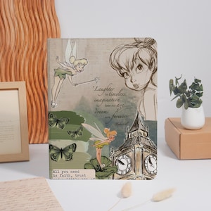 Pode incluir: Um caderno retangular com ilustrações da Sininho, borboletas verdes e um esboço do Big Ben. A capa inclui o texto: Laughter is timeless, imagination has no age, dreams are forever, e All you need is faith, trust and a little bit of.