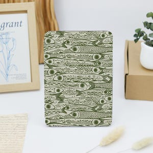 May include: A rectangular tablet or e-reader case featuring a repeating pattern of olive green fish on a light beige background. The fish are depicted in a stylized, graphic manner with dotted textures and circular eyes, covering the entire surface.