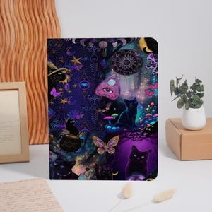 May include: A notebook with a fantasy illustration featuring black cats, butterflies, mushrooms, and a Ouija planchette against a dark purple and blue starry background. The design includes moons, stars, and a mystical forest theme.