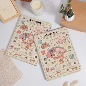K&ouml;nnte beinhalten: Zwei beige Tablet-H&uuml;llen mit einem Cartoon-Anatomie-Design. Das Design zeigt eine rosa und wei&szlig;e Figur mit anatomischen Illustrationen, Wolken und Sternen. Die Texte "ANATOMY" und "LEMONBOY" sind sichtbar.