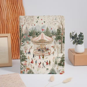 May include: A rectangular notebook featuring a detailed illustration of a winter carousel scene. The artwork depicts a pink and white carousel surrounded by snow-covered pine trees, festive hanging ornaments, and small figures in winter clothing.
