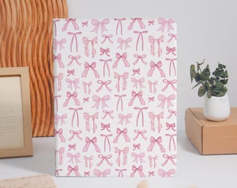 May include: A rectangular tablet case featuring a repeating pattern of light pink bows on a white background. The bows vary in size and orientation, creating a consistent graphic design across the entire surface of the protective cover.