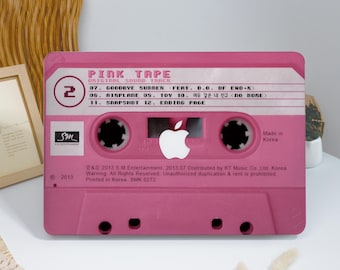 May include: A pink cassette tape design with the text "PINK TAPE" and track listings. Features the Apple logo in the center. The design includes the text "Made in Korea" and "2013".