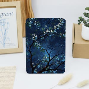 May include: A rectangular tablet case featuring a dark blue background with a tree design. The tree has dark brown branches and is adorned with white and light blue flowers. The case is designed to protect a tablet.