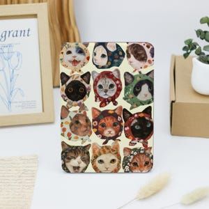 May include: A collage of 15 cat faces, each wearing a different patterned fabric over their heads. The cats are all looking at the camera with different expressions. The background is a light yellow.