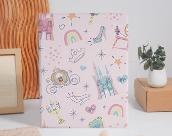 May include: A rectangular tablet case with a light pink background featuring a repeating pattern of fairy tale icons including castles, a pumpkin carriage, a glass slipper, rainbows, crowns, hearts, stars, and a candelabra in pastel colors.