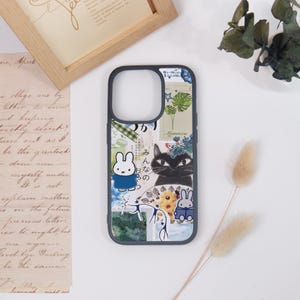 May include: A phone case with a collage design featuring a black cat, a white bunny, and Japanese text. The case has a dark blue border and a mix of floral and vintage paper elements in the background.