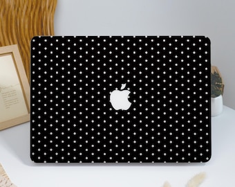 May include: Black laptop case with a white polka dot pattern. The Apple logo is centered on the case. The case is on a white surface with a wooden frame and decorative elements in the background.