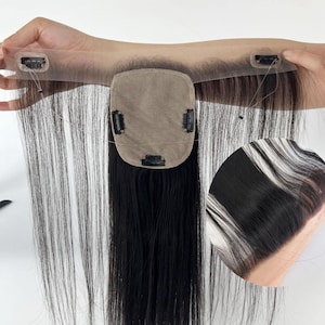Pode incluir: Um topper de cabelo preto com uma pequena base quadrada e longas mechas de cabelo liso. O topper tem clipes para fixação e uma fina renda transparente na frente. O cabelo parece ser de uma cor preta natural.