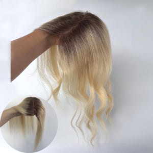 Puede incluir: Una pieza de cabello rubio con raíces oscuras y puntas onduladas. La pieza de cabello se sostiene sobre un fondo blanco, mostrando su color y textura. Una imagen más pequeña insertada muestra la pieza de cabello desde otro ángulo.