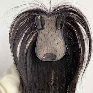 May include: A dark brown hair topper with a lace base and clips for attachment. The hairpiece has long, straight strands and is designed to add volume and coverage. The base is a neutral colour, and the clips are black.