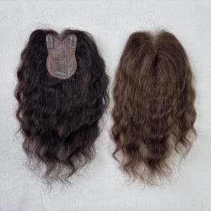 Pode incluir: Duas perucas com texturas onduladas. Uma é castanho escuro com base e presilhas castanhas, a outra é castanho claro. Ambas são projetadas para adicionar volume e comprimento ao cabelo natural.