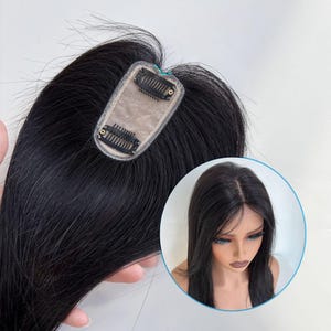 Puede incluir: Un postizo de cabello negro con una base de encaje y clips para sujetar. El cabello es largo y liso, con una raya de aspecto natural. Una imagen más pequeña muestra el cabello en una persona.