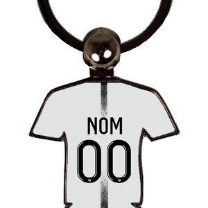 May include: A white jersey-shaped keychain with the text "NOM" above the number "00" in black. The keychain has a black ring and a silver-colored ball at the top. The team logo is at the bottom.