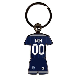 May include: A navy blue soccer jersey keychain with the word "NOM" and the number "00" in white. The keychain has a silver ring and a small ball at the top.