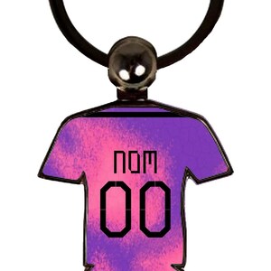 May include: A purple and pink jersey-shaped keychain with the word "NOM" and the number "00" printed on the front. The keychain has a black ring and a small, round, silver-colored attachment.