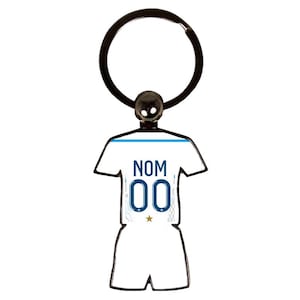Peut inclure: Un porte-clés blanc et bleu en forme de maillot de football. Le maillot porte le mot "NOM" et le numéro "00". Le porte-clés a un anneau noir et une petite boule noire en haut.