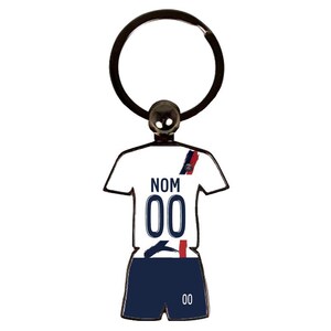 May include: A metal keychain in the shape of a soccer jersey and shorts. The jersey is white with the word "NOM" and the number "00" printed on it. The shorts are navy blue with the number "00" printed on them. The keychain has a black ring.