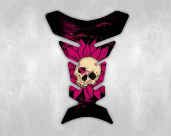May include: A motorcycle tank protector with a black and pink design. The graphic features a skull with a pink flower and leaf design. The top and bottom of the protector are black.
