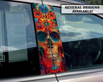 Op de afbeelding: Een kleurrijke auto raam sticker met een schedel met bloemmotieven. De sticker is in tinten rood, oranje, blauw en groen. De tekst "SEVERAL DESIGNS AVAILABLE!" wordt boven de sticker weergegeven.