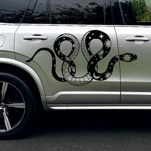 May include: Black snake decal with celestial accents, including stars and crescent moons. The snake design is applied to the side of a silver vehicle, creating a unique and eye-catching aesthetic. The snake's body is detailed with scale patterns.
