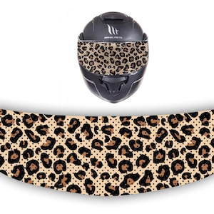 Può includere: Un casco da moto nero con una visiera a stampa leopardata e una mentoniera a stampa leopardata. Il casco è su uno sfondo bianco.