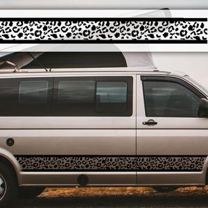 May include: A silver van with black leopard print decals. The decals are horizontal stripes with a black border and a pattern of black spots on a white background. The decals are on the side of the van.