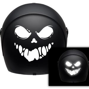 Puede incluir: Un casco de moto negro con un diseño de calavera y huesos cruzados reflectantes blancos. El diseño es visible en la oscuridad.