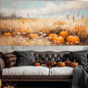 May include: A rectangular canvas painting shows pumpkins and wildflowers in a field under a cloudy sky. A brown leather sofa with cushions and pumpkins is in front of the painting. A carved pumpkin sits on the floor.